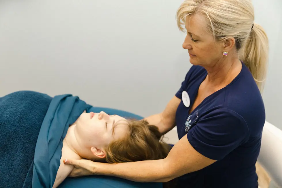 A therapist working through a head and neck massage on navy linens