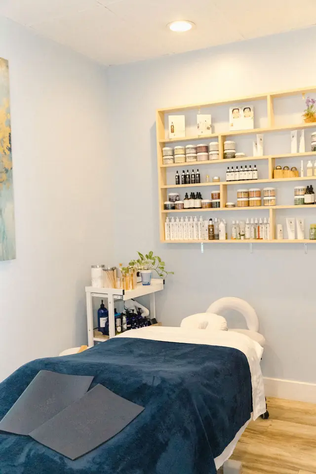 A treatment room with a navy blanket on the table and shelves of skincare